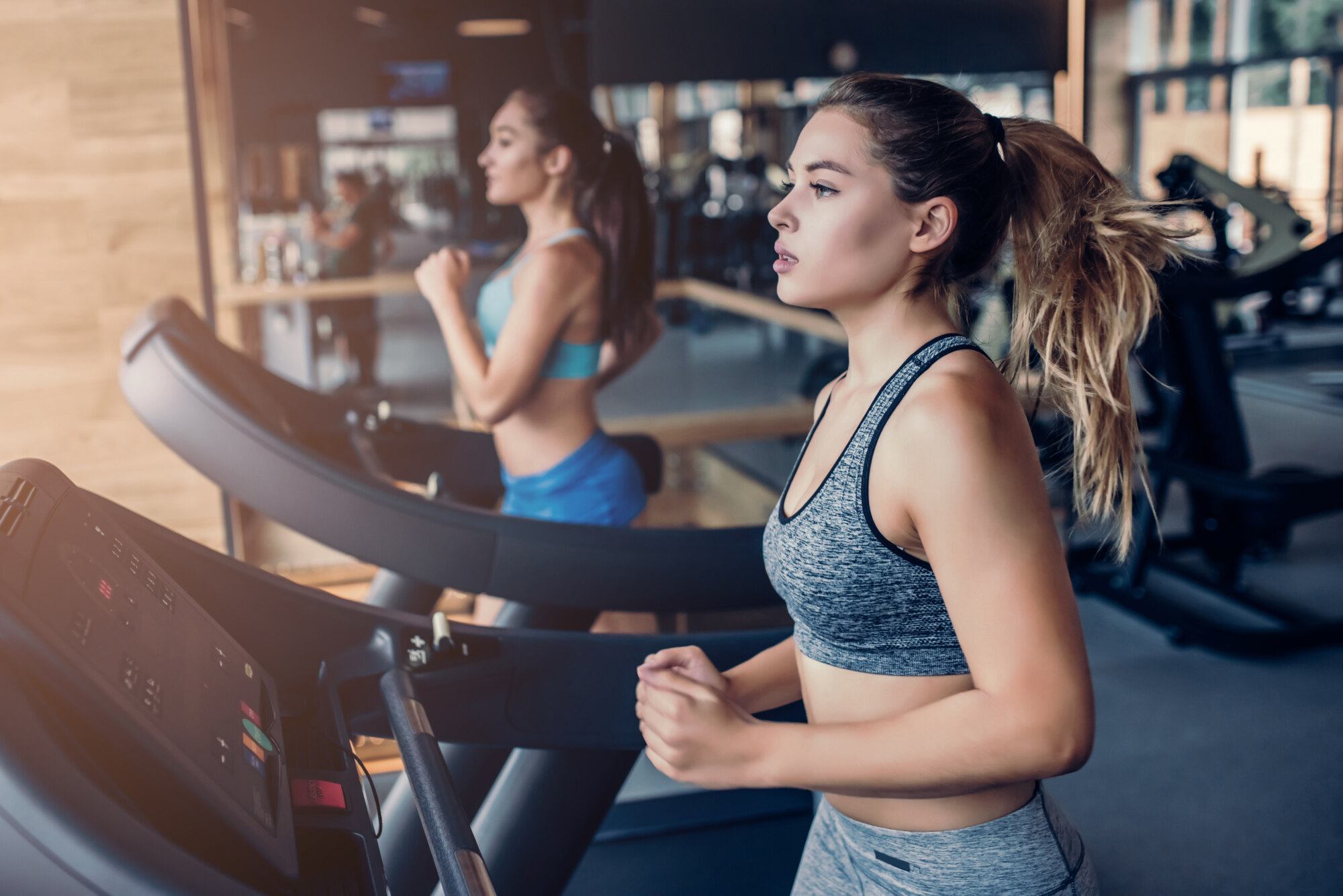 Side view of two attractive sports women on running track. Girls on treadmill