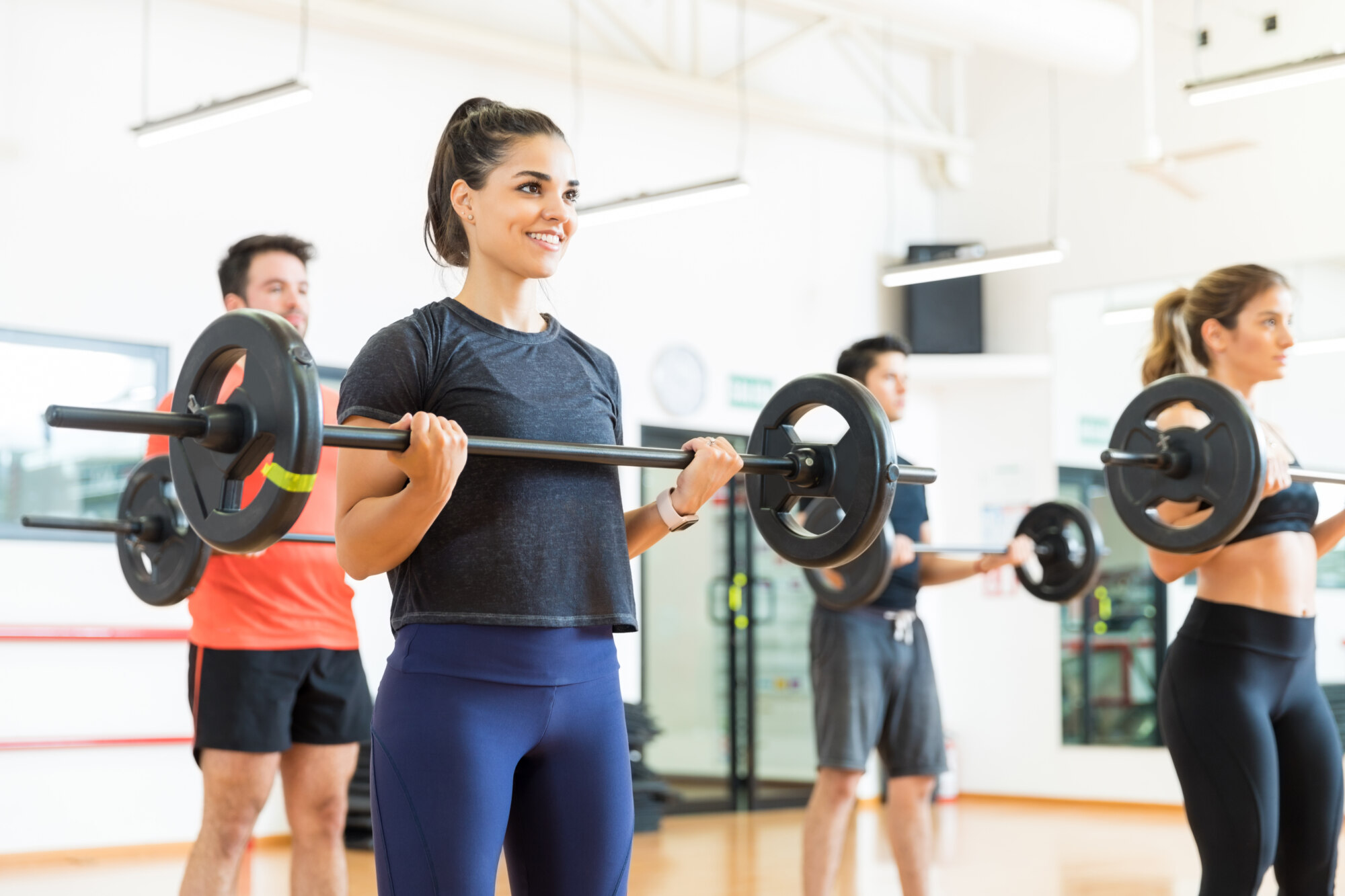 Young woman smiling while lifting barbell by friends in health club